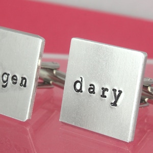 May include: A pair of silver cufflinks with the words "legendary" and "dary" engraved on them.