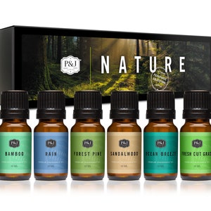 May include: Set of six 10 ml amber glass bottles with black caps, containing essential oils. The bottles are labeled with the names "Bamboo", "Rain", "Forest Pine", "Sandalwood", "Ocean Breeze", and "Fresh Cut Grass". The bottles are arranged in a row on a white background. The bottles are part of a "Nature" fragrance collection.