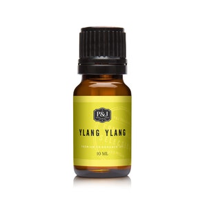 May include: A 10 ml amber glass bottle of Ylang Ylang essential oil with a black screw-on cap. The label is yellow with black text that reads "P&J Trading, Premium Fragrance Oil, Ylang Ylang Selection, 10 ml".