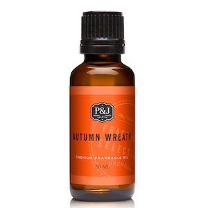 May include: A 30 ml amber glass bottle with a black cap. The label is orange with black text that reads "P&J Trading", "Autumn Wreath", "Fragrance Oil", "Premium", and "30 ml".