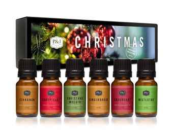 May include: A set of six 10 ml bottles of essential oil in a box with a Christmas tree and ornaments design. The bottles are labeled with Christmas scents: Cinnamon, Candy Cane, Christmas Wreath, Gingerbread, Cranberry, and Mistletoe.