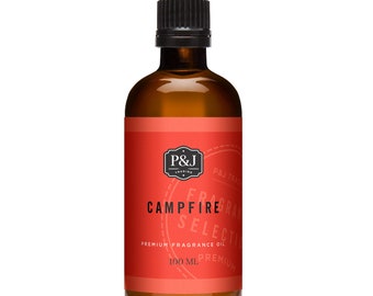 Op de afbeelding: Een flesje van 100 ml Campfire geurolie. De fles is van amberkleurig glas met een zwarte dop. Het etiket is rood met witte tekst en een zwart-wit logo. De tekst op het etiket luidt "P&J Trading", "Campfire", "Fragrance Selection", "Premium Fragrance Oil", "100 ml" en "Premium".