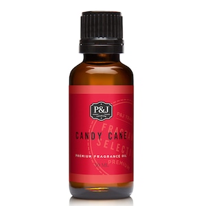 May include: A 30 ml bottle of Candy Cane fragrance oil. The bottle is amber glass with a black cap. The label is red with white text and a black and white logo. The text on the label reads "P&J Trading, Candy Cane Selection, Premium Fragrance Oil, 30 ml, Premium".