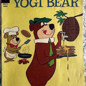 May include: A vintage comic book cover featuring Yogi Bear and Boo Boo Bear. The cover is yellow with a red and green title that reads "Hanna-Barbera Yogi Bear". Yogi Bear is wearing a green hat and a green scarf. He is holding a plate of pancakes with syrup dripping down. Boo Boo Bear is wearing a chef's hat and apron and is cooking pancakes over a fire.