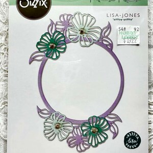 May include: A purple and green floral die cut frame with the text "FRAMELITS®" and "LISA JONES" on a white background. The die cut is for use with a die cutting machine. The package includes 4 dies. The price is $19.99.