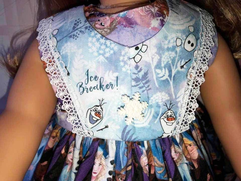 K&ouml;nnte beinhalten: Hellblaues Kleid mit wei&szlig;er Spitzenborte und V-Ausschnitt. Das Kleid zeigt einen Aufdruck von Figuren aus dem Film Frozen, darunter Olaf, Schneeflocken und den Text "Ice Breaker!"