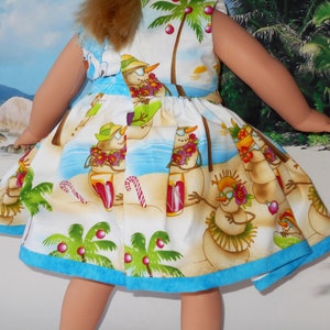 Pode incluir: Um vestido branco com uma bainha azul apresenta uma cena de praia tropical com bonecos de neve usando colares de flores e segurando bebidas. O vestido tem um tema natalino festivo com palmeiras e enfeites vermelhos.