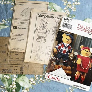 May include: Simplicity craft pattern featuring teddy bears in outfits. The pattern includes instructions and diagrams for creating the bears and their clothing. The cover shows two finished bears, one in a sweater and the other in a red dress.