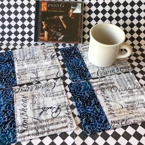 May include: Four blue and white fabric coasters with musical notes and the words "Symphony", "Orchestra", and "Concert" printed on them. The coasters are sitting on a black and white checkered surface.