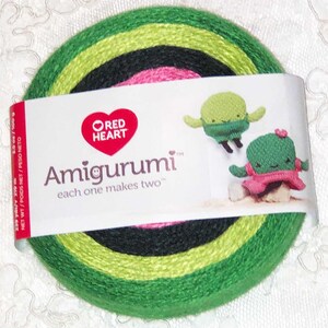 May include: A skein of green, black, and pink yarn with a label that reads "Red Heart Amigurumi, each one makes two". The label also features two crocheted amigurumi cactus toys.