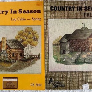 May include: Two vintage cross-stitch kits titled "Country In Season." One features a log cabin scene with the text "Log Cabin - Spring." The other depicts a fall barn scene. Both kits are by Creative Keepsakes.