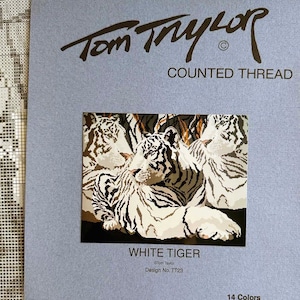 May include: A counted cross stitch pattern featuring three white tigers huddled together. The pattern is titled "White Tiger" by Tom Taylor and has 14 colors, 125 x 180 stitches. It is produced by FineArts Graphics.