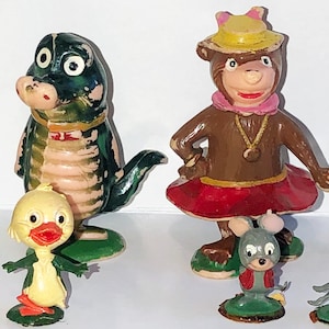 May include: A set of seven vintage plastic figurines, including a yellow duck, a green alligator, a brown bear wearing a yellow hat and red skirt, a brown bear wearing a green hat and scarf, and two gray mice.