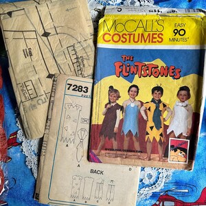 May include: Vintage McCall's Costumes sewing pattern for The Flintstones. The pattern packet features images of children dressed as characters from the cartoon. Includes pattern pieces and instructions. The pattern is marked "Easy 90 Minutes".