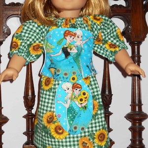 May include: A doll wearing a green and white gingham dress with a blue and white fabric panel featuring a scene from the movie Frozen. The dress has sunflowers printed on it. The doll is wearing black shoes.