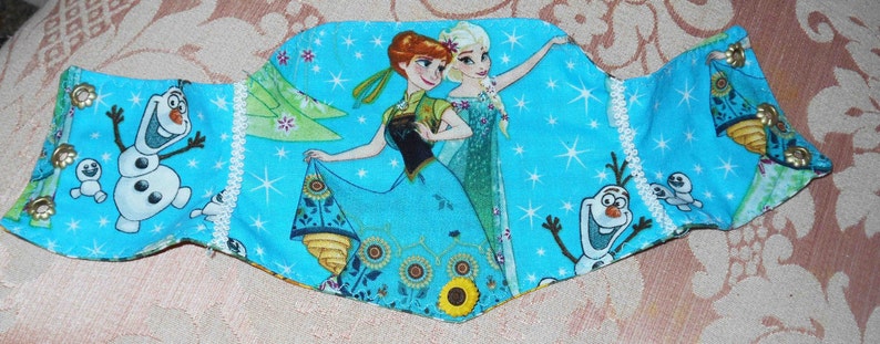 May include: A blue fabric headband with a white lace trim and a colorful print featuring characters from the movie Frozen. The print includes Elsa, Anna, Olaf, and a snowflake design.