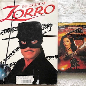May include: A DVD cover for the movie "The Legend of Zorro" featuring Antonio Banderas and Catherine Zeta-Jones. The cover has a red background with a black and white image of Zorro on a horse.