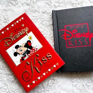 May include: Two red hardcover books with gold lettering. The book on the left has a picture of Mickey Mouse and Minnie Mouse kissing. The book on the right has the title "The Disney Kiss".