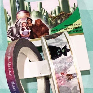 May include: Two rolls of washi tape featuring images from the Wizard of Oz. One roll has a black and white image of Dorothy, the Scarecrow, the Tin Man, and the Cowardly Lion. The other roll has a colorful image of the Wicked Witch of the West. The text on the packaging reads "The Wizard of Oz" and "washi tape, cinta adhesiva washi, ban washi".