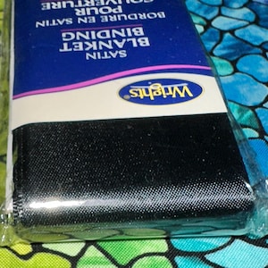 May include: A package of black satin blanket binding. The label reads "Satin Blanket Binding" and "Wright's" in a blue and white oval. The binding is wrapped in clear plastic.