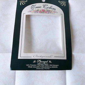 May include: A white package with black trim for True Colors Sponged #28 Even Weave fabric. The package is labeled "True Colors" and "Backgrounds". The fabric is 100% polyester and is recommended to be washed in cold water with mild detergent. The package is made by True Colors Publishing & Design in Chattanooga, TN 37421.