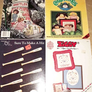 May include: Four cross stitch pattern books. The first book features a Christmas stocking with the text "Hartley Little People Spread Great Joy". The second book features Cabbage Patch Kids with the text "Cabbage Patch Kids". The third book features baseball bats with the text "Sure To Make A Hit". The fourth book features a pillow with the text "Ziggy by Tom Wilson".