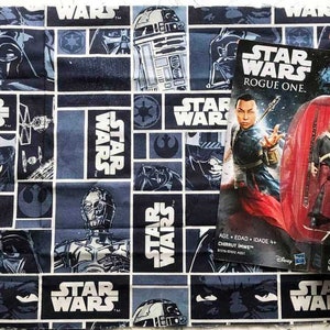 May include: A Star Wars themed fabric with a repeating pattern of characters and the words "Star Wars". The fabric is blue and white with images of Darth Vader, R2-D2, and other characters. A Star Wars action figure is displayed on the fabric.