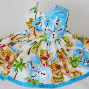 Pode incluir: Um vestido branco sem mangas com uma bainha azul. O vestido apresenta uma estampa tropical com palmeiras, bonecos de neve e os personagens Olaf e Sven do filme Frozen.