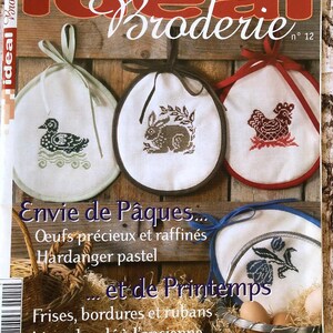 May include: A magazine cover titled Ideal Broderie no 12 featuring three round white fabric ornaments with cross-stitch designs of a duck, a rabbit, and a chicken, each with a colored ribbon loop, plus text including Envie de Pâques.