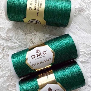 May include: Three spools of DMC Diamant embroidery thread in a dark green color with a metallic sheen. The spools are labeled with the DMC logo and the text "Diamant" in gold lettering. The spools are 35 meters long.