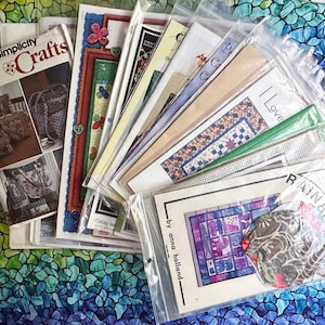 May include: A stack of various quilting and craft patterns in plastic bags. The patterns include a variety of designs, including a rainbow, a heart, and a butterfly. The patterns are labeled with the names "Simplicity Crafts", "I Love", and "Rainbow".