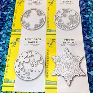 May include: Four die-cut paper craft designs with snowflake patterns. The designs include three Snowy Circle layers and one Pinpoint Snowflake. Each design is on a yellow and white card with the text "BIRCH PRESS DESIGN".