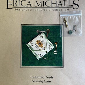 May include: A cross stitch pattern for a sewing case with the title "Treasured Tools Sewing Case". The pattern includes a small white and green fabric with a keyhole design and a key charm. The pattern also includes brass charms, a hand-dyed button, linen thread, and instructions for stitching and finishing.