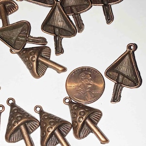 May include: Bronze-colored mushroom charms with a loop for jewelry making. The charms have a detailed cap and stem design. A US penny is included for size reference. These charms are ideal for crafting and DIY projects.