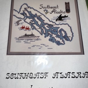 May include: Cross-stitch pattern of Southeast Alaska, featuring a map with blue waterways, a whale, and a totem. The words "Southeast Alaska" are displayed above the map. The image includes instructions.