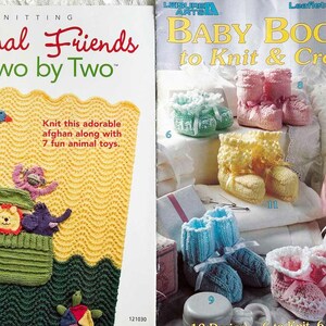 May include: Two knitting pattern books, one titled "Animal Friends Two by Two" with a yellow and green knitted baby blanket with animal toys, and the other titled "Baby Booties to Knit & Crochet" with a variety of knitted baby booties in pink, blue, yellow, and white.