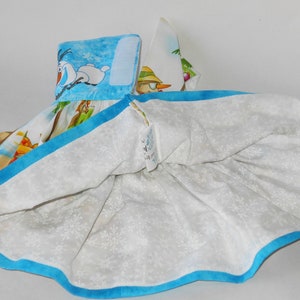 Pode incluir: Um vestido branco com uma bainha azul e uma estampa colorida com personagens do filme Frozen. A estampa inclui Olaf, Elsa e Anna.