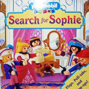 May include: A colorful children's book with the title "Search for Sophie" and illustrations of dolls in a room with a mirror and a chair. The book has flaps, pull-tabs, and pop-ups.