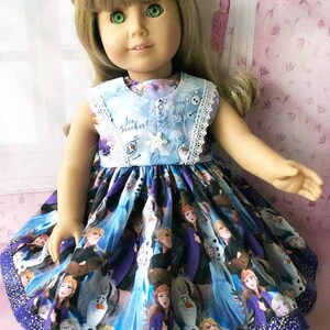 K&ouml;nnte beinhalten: Eine Puppe in einem blau-violetten Kleid mit Frozen-Motiv. Das Kleid zeigt Charaktere aus dem Film, darunter Elsa und Olaf. Das Oberteil hat den Text "Ice Breaker!" und eine wei&szlig;e Spitzenborte.