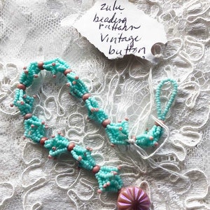 May include: A turquoise and pink beaded necklace with a vintage purple button. The necklace is made with small seed beads and has a delicate, intricate design. The button is a beautiful accent piece.