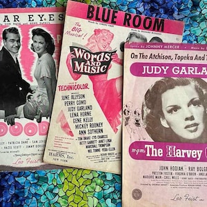 May include: Three vintage sheet music covers featuring Judy Garland, Red Skelton, and June Allyson. The covers are in various shades of pink, blue, and white with black text. The titles are "Star Eyes", "Blue Room", and "On The Atchison, Topeka And The Santa Fe".