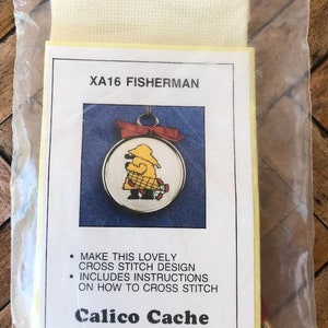 May include: A yellow and red cross stitch kit with a fisherman design. The kit includes instructions on how to cross stitch. The kit is from Calico Cache, Eagle River, Alaska. © Naomi Leonard 1988.