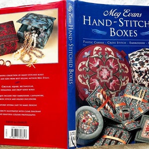 May include: A book titled "Meg Evans Hand-Stitched Boxes" with a blue cover and a photo of various hand-stitched boxes on the front. The book cover text also includes "Plastic Canvas, Cross Stitch, Embroidery, Patchwork". The back cover shows a red box with a blue lid and a photo of jewelry inside.
