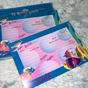May include: A pack of 36 recipe cards featuring a tropical ocean theme. The cards are blue with pink and white bubbles and colorful fish. The text on the cards reads "36 Recipe Cards", "Recipe", "From", "Cooking Time", "Serves", "Preheat Oven To", "Bermuda".