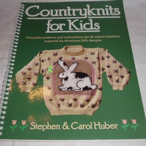 May include: A spiral-bound book titled "Countryknits for Kids" with a green cover. The cover features a knitted sweater design with a rabbit motif. The book contains patterns and instructions for 25 casual sweaters inspired by American folk designs. The authors are Stephen & Carol Huber.