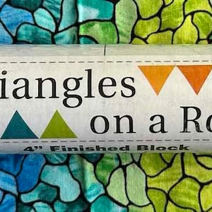 May include: A white roll of fabric with a label that says "Triangles on a Roll" and features a colorful triangle design. The label also states "4" Finished Block".