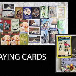 May include: A collection of playing cards with various designs, including a deck featuring a lion, a deck with a tropical island theme, and a deck with a cityscape. The cards are arranged in a grid pattern on a white surface.