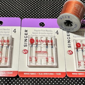 May include: Three identical packages of Singer regular point universal sewing machine needles, each containing four needles marked size 90/14, alongside a single spool of copper-colored thread with a label indicating 300 yards and 274 meters.
