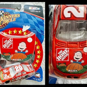 May include: A red NASCAR die-cast car with a number 20 on the side. The car is sponsored by The Home Depot and features a Peanuts character, Snoopy, on the hood. The car is part of the Winner's Circle collection.