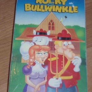 May include: A VHS tape cover featuring the cartoon characters Rocky and Bullwinkle. The cover is blue with white text that reads "The Adventures of Rocky and Bullwinkle". The characters are depicted in front of a wooden house with a red roof. The text "Canadian Gothic" is on a gold banner at the bottom of the cover.